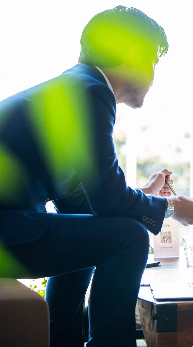 窓際のカフェで、ビジネススーツ姿の男性とエプロン姿の女性たちが打ち合わせをしている様子