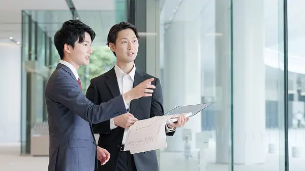 ビジネス風の服装の3人がテーブル越しにノートパソコンを見ながら話し合っている打ち合わせの様子